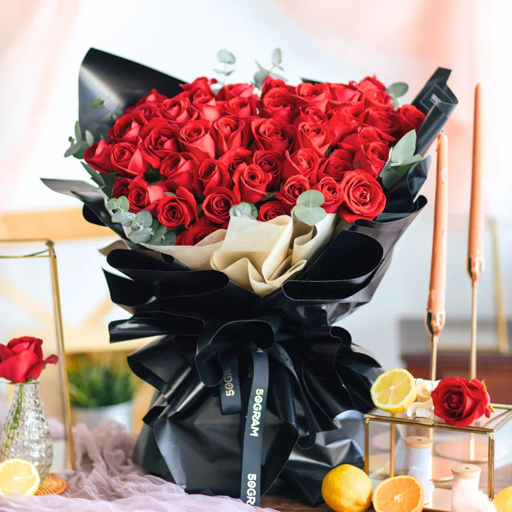 Elegant hand bouquet of fresh red roses with greenery in black wrap, gift arrangement