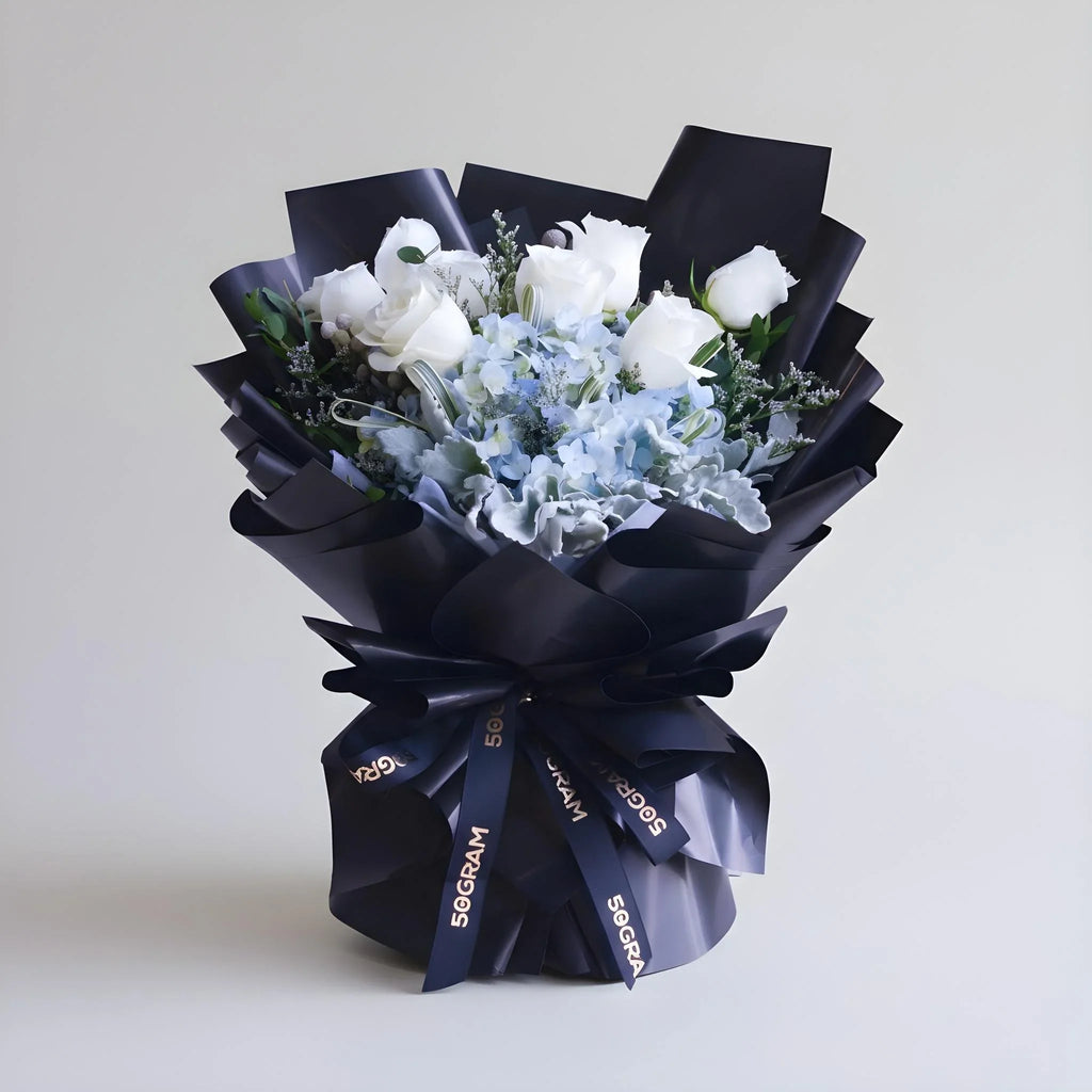 Elegant bouquet of white roses and blue hydrangeas wrapped in black paper with ribbon
