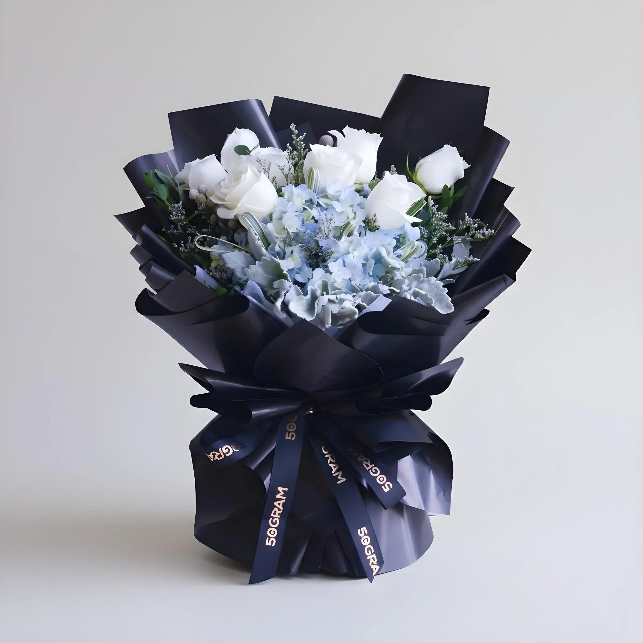 Elegant bouquet of white roses and blue hydrangeas wrapped in black paper with ribbon