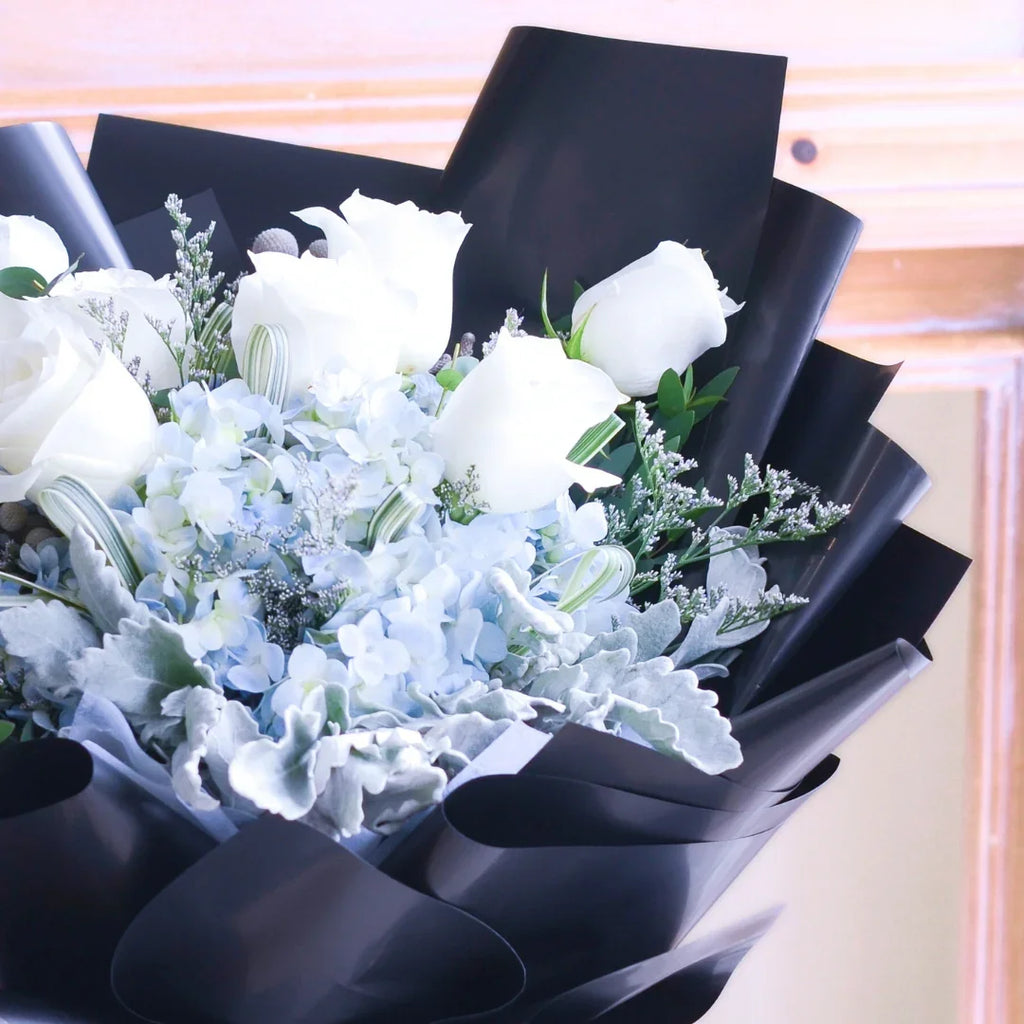 Elegant bouquet of white roses and blue hydrangeas wrapped in black paper