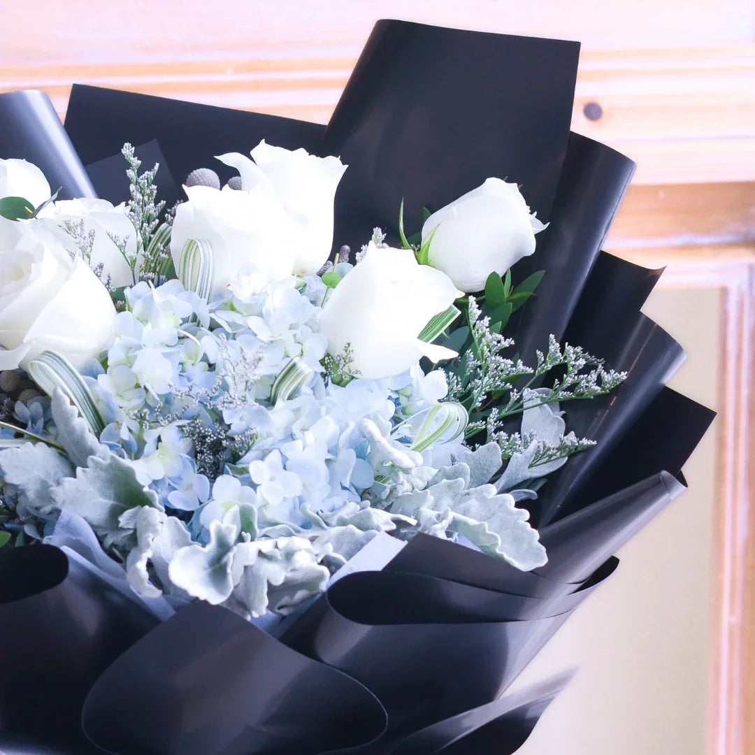 Elegant bouquet of white roses and blue hydrangeas wrapped in black paper