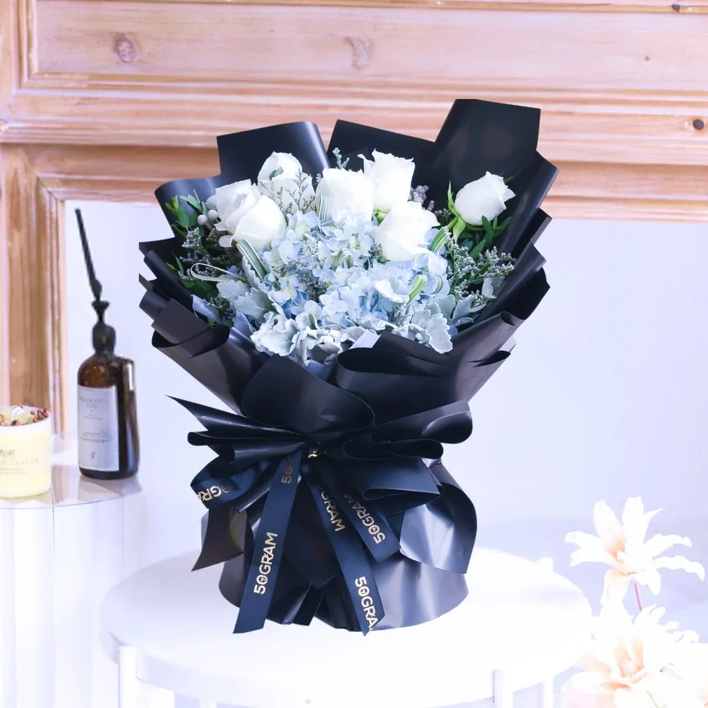 Elegant bouquet of white roses and blue hydrangeas wrapped in black ribbon arrangement