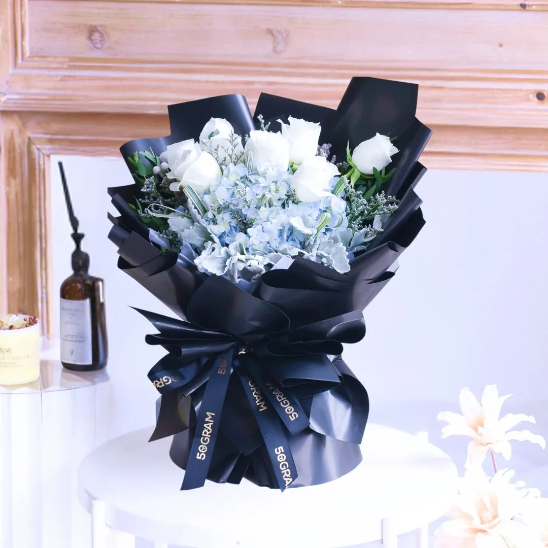 Elegant bouquet of white roses and blue hydrangeas wrapped in black ribbon arrangement