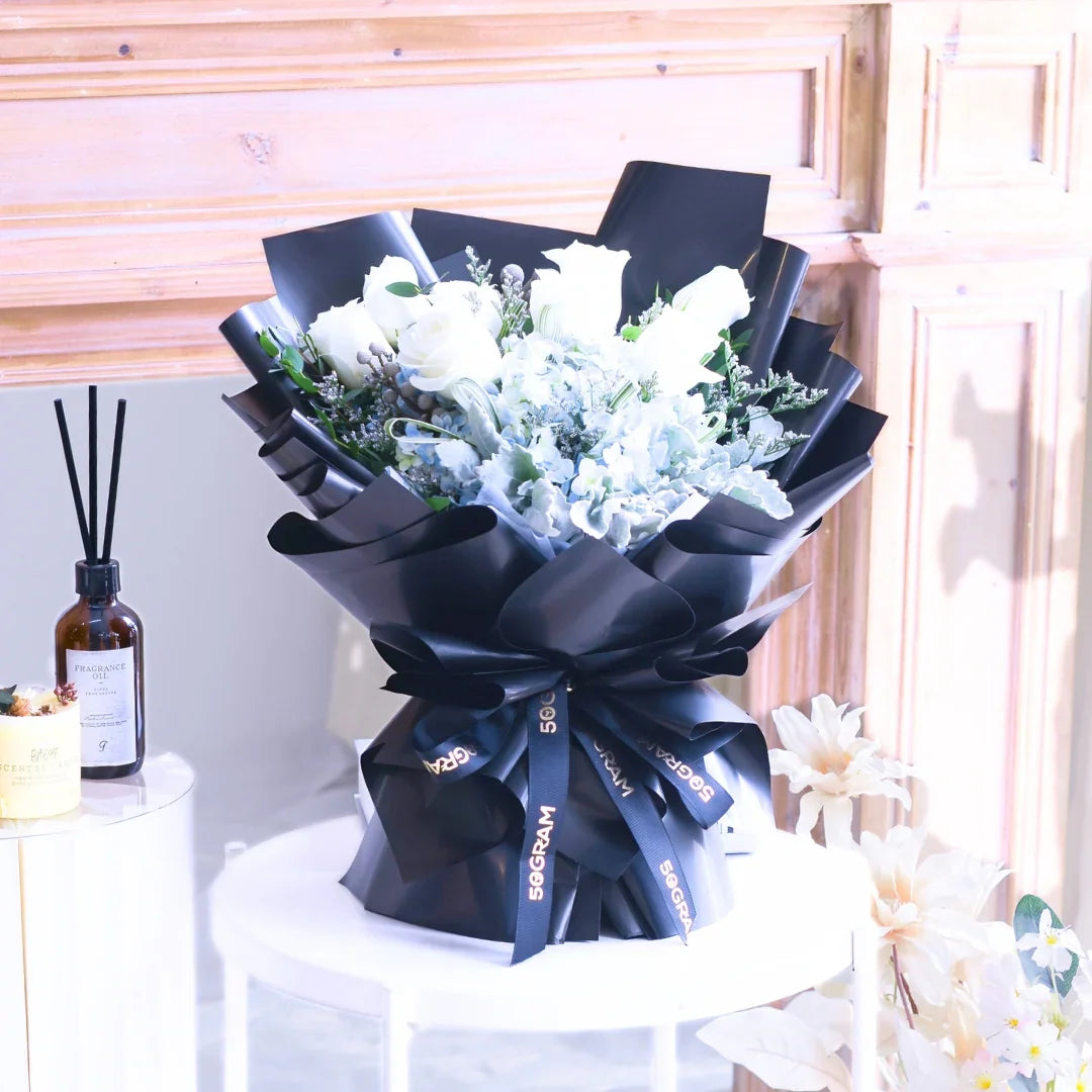 Elegant bouquet of white roses and blue hydrangeas wrapped in black paper on a table