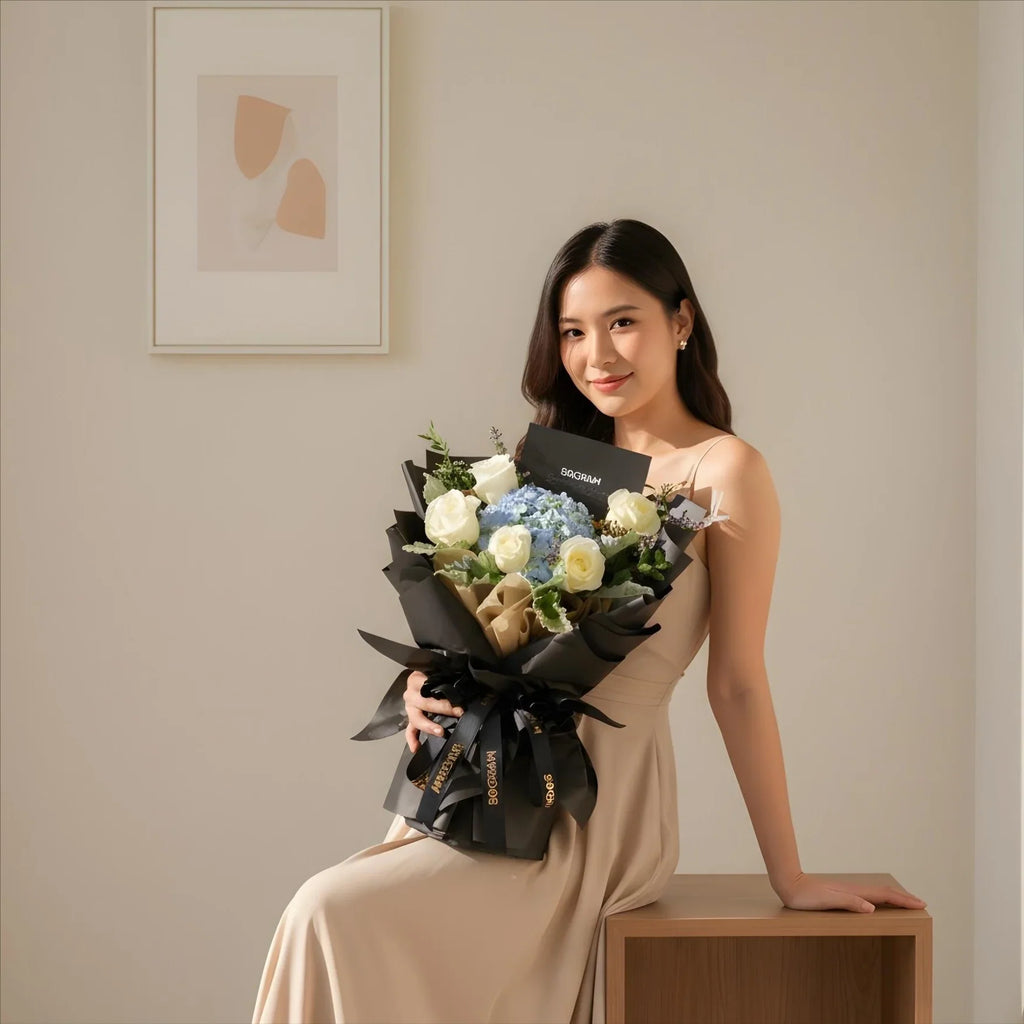 Woman in beige dress holding elegant bouquet with white roses and blue hydrangeas indoors