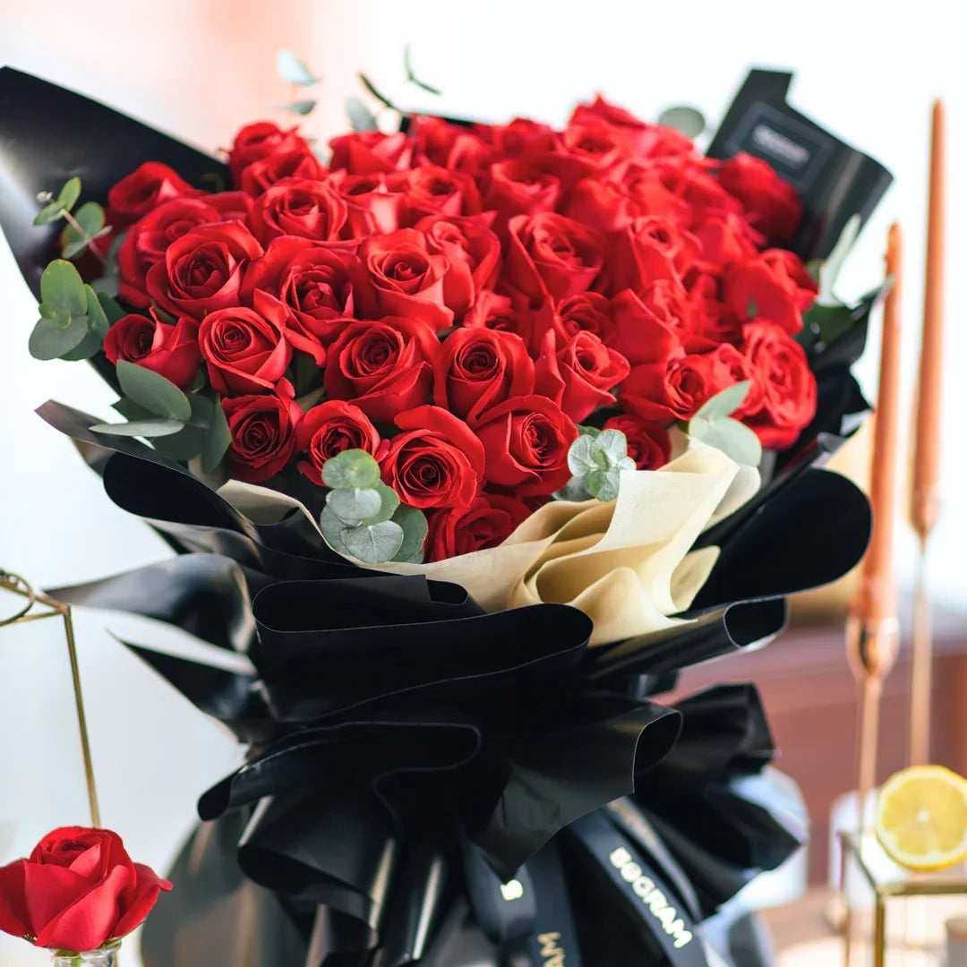 Large hand bouquet of fresh red roses wrapped in black and beige paper with eucalyptus leaves