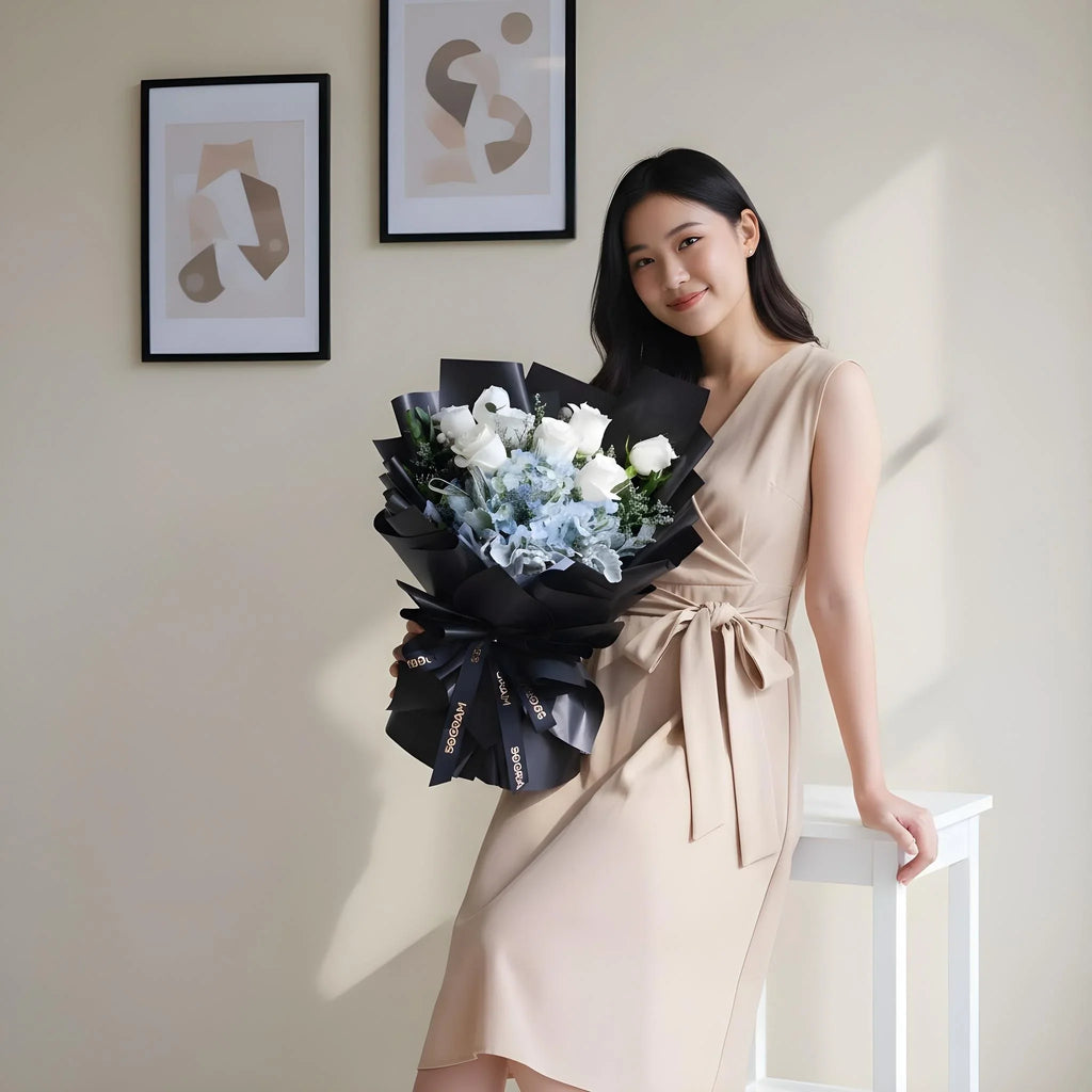 Woman in beige dress holding elegant black-wrapped bouquet of white roses and blue hydrangeas